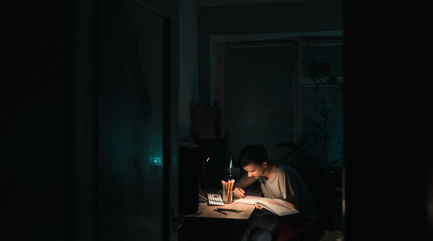 Seseorang bekerja dengan kertas di meja di bawah lampu pada malam hari